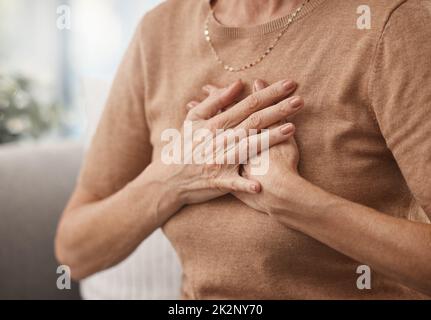 Call the doctor in case of emergency. Shot of an unrecognisable woman experiencing chest pain at home. Stock Photo