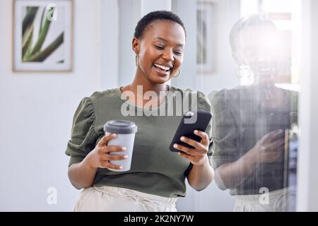 I needed a good distraction from my hectic schedule. Shot of a businesswoman drinking coffee and using her cellphone while standing in an office. Stock Photo