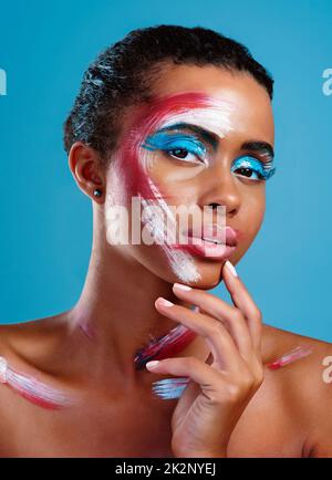 Well...colour me intrigued. Studio portrait of a beautiful young woman covered in face paint posing against a blue background. Stock Photo