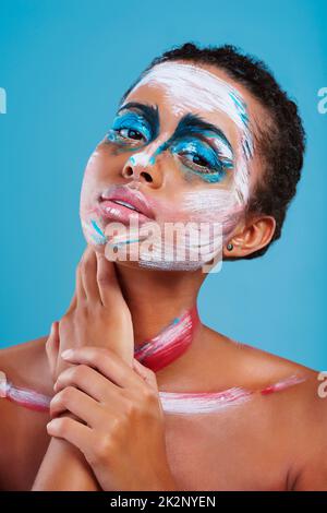 Sometimes youve just gotta stand out. Studio portrait of a beautiful young woman covered in face paint posing against a blue background. Stock Photo