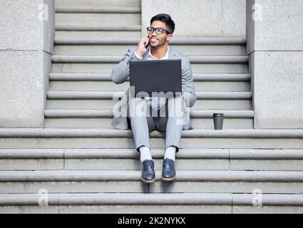 Another successful business call. Shot of a young businessman using a laptop while on the phone in the city. Stock Photo
