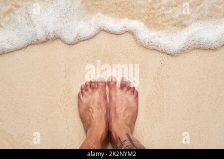 Salty hair and sandy toes. High angle shot of a mans feet at the beach. Stock Photo