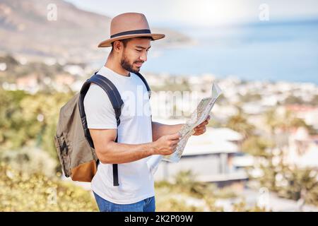 Im not lost, Im just exploring. Shot of a young man holding a map while exploring outdoors. Stock Photo