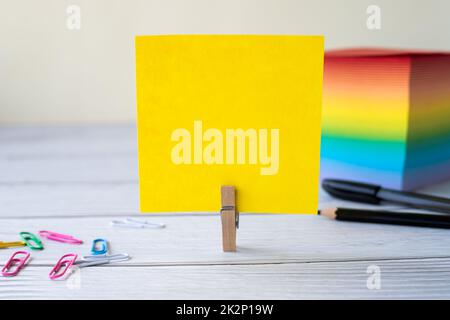 Blank Sticky Note With Laundry Clip Stack Of Colorful Paper Pen Placed On Table. Empty Piece Of Sheet Clipped Beside Pen And Flashy Papers On Desk. Stock Photo