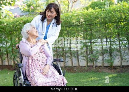 Doctor help and care Asian senior or elderly old lady woman patient sitting on wheelchair at park in nursing hospital ward, healthy strong medical concept. Stock Photo