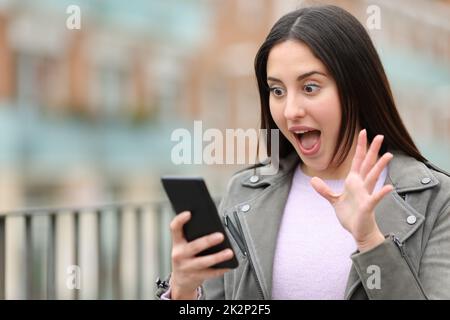 Surprised woman checking cell phone in the street Stock Photo