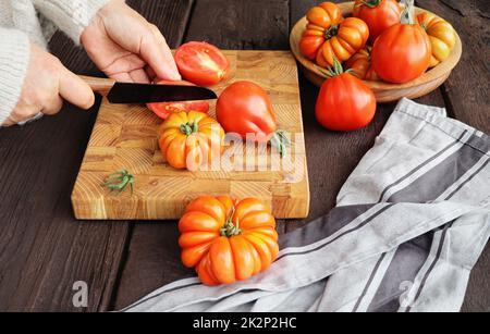 Fresh ripe hairloom tomatoes and knife on rustic wooden board over dark background Stock Photo