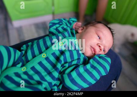 Infant baby in striped clothes lies with arms raised up Stock Photo