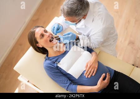 Male Dentist Treating Teeth Of Young Pregnant Woman Stock Photo