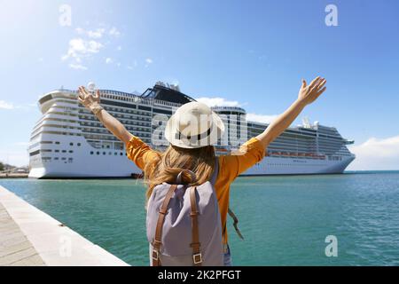 Back view of traveler girl with raised arms standing in front of big cruise liner Stock Photo