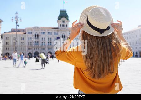 Tourism in Europe. Back view of pretty girl holding hat in Trieste, Italy. Beautiful young woman visiting Europe. Stock Photo