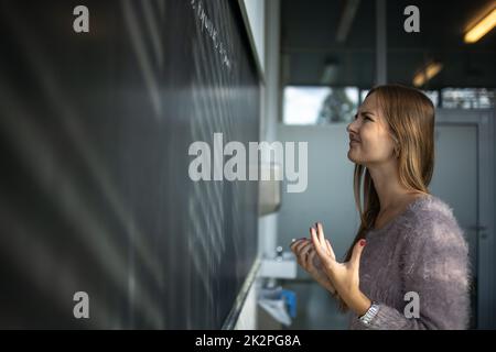 Pretty, young female student in front of a blackboard during math class Stock Photo