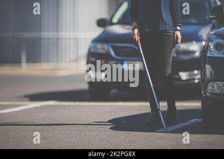 Blind woman walking on city streets, using her white cane to navigate the urban space better and to get to her destination safely Stock Photo