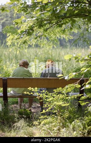 Elderly couple outdoors in summer. Happy elderly couple on a walk. Handsome man and woman senior citizens. Husband and wife of old age against the background of nature. Stock Photo