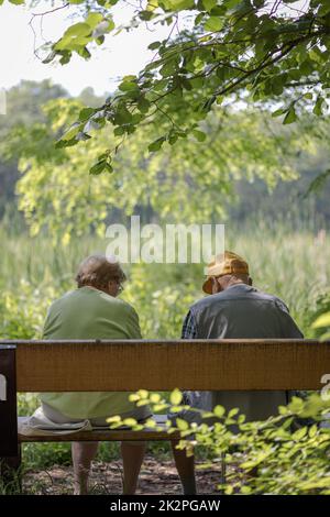 Elderly couple outdoors in summer. Happy elderly couple on a walk. Handsome man and woman senior citizens. Husband and wife of old age against the background of nature. Stock Photo
