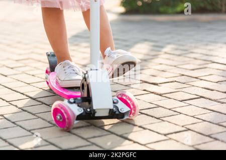 Happy Asian little kid girl wear safe helmet playing pink kick board on road in park outdoors on summer day Stock Photo