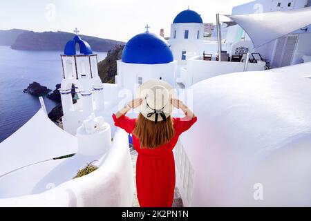 Holidays in Santorini. Back view of traveler woman descends stairs in the traditional village of Oia with blue domes churces and with houses on Santorini Island. Stock Photo