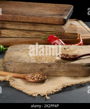 empty kitchen brown wooden cutting board on black table, next to spoons with spice and fresh chili, black background Stock Photo