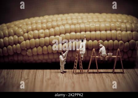 Miniature painters coloring corn on the cob Stock Photo