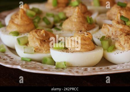 Deviled eggs with cod livers with leek on white plate. Rustic wooden table Stock Photo