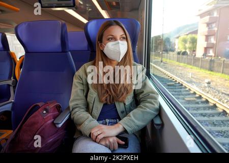 Young female backpacker traveling by train with protective face mask Stock Photo