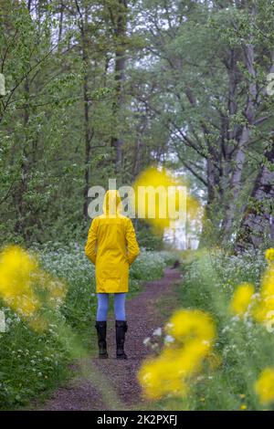 Young woman with yellow raincoat and rubber boots in spring nature Stock Photo