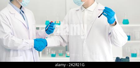 Covid-19 testing in laboratory. Two scientists hand shake while holding blood samples of patients infected with Coronavirus disease 2019. Healthcare and medical banner background concept. Stock Photo