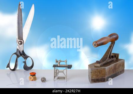 Professional old large tailor scissors, large tailor iron miniature model of a sewing machine and accessories on table with blue background. Advertisment for tailor business. Space for text and montage. Stock Photo