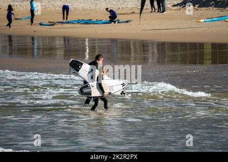 A rear shot of surfers holding shortboards and going back to the beach wearing black suits Stock Photo