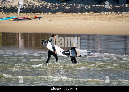 A rear shot of surfers holding shortboards and going back to the beach wearing black suits Stock Photo