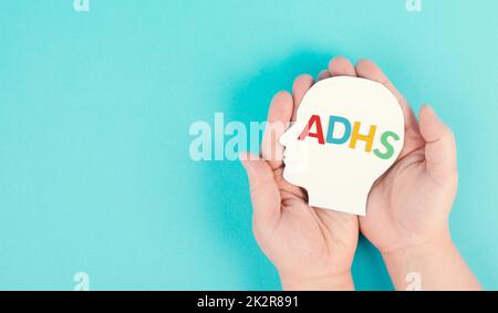 Hands holding a head with the german word ADHS which means attention deficit hyperactivity disorder, ADHD symptom, mental health Stock Photo