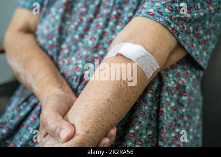 Asian senior or elderly old lady woman patient show cotton wool stop bleeding, after blood drawing testing for annually physical health check up to check cholesterol, blood pressure, and sugar level. Stock Photo