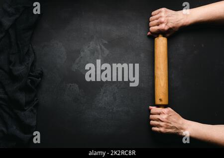 https://l450v.alamy.com/450v/2k2rc8r/two-female-hands-hold-a-wooden-rolling-pin-for-rolling-dough-on-a-black-table-top-view-place-for-an-inscription-2k2rc8r.jpg