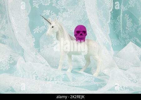a shiny white unicorn carrying a plastic skull on its back Stock Photo
