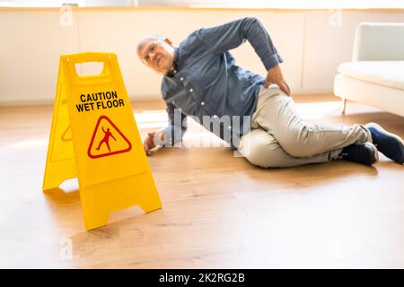 Man Falling On Wet Floor In Front Of Caution Sign Stock Photo