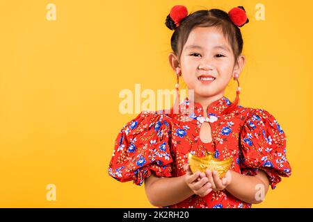 Happy Asian Chinese little girl smile wearing red cheongsam holding gold ingot Stock Photo