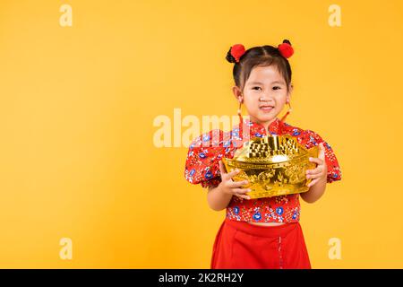 Happy Asian Chinese little girl smile wearing red cheongsam holding big gold ingot Stock Photo
