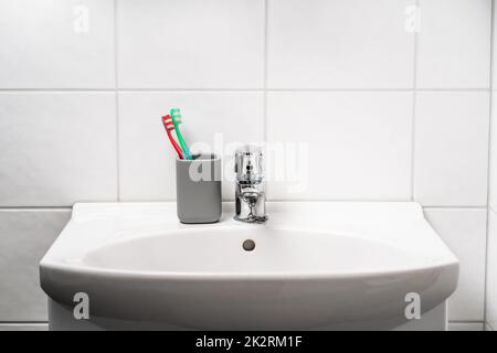 Toot brush cup in bathroom and toilet sink. Toothbrush in clean restroom. Water tap, faucet and basin to wash hands in WC. Glass jar. Dental hygiene. Stock Photo