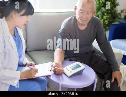 Asian caregiver doctor examine older patient use blood pressure gauge. Stock Photo