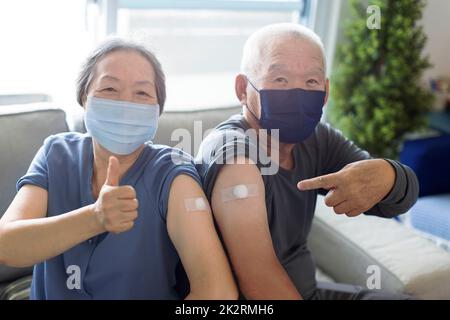 Senior couple wearing face mask virus protection and showing bandage injection covid-19 vaccinated with thumb up