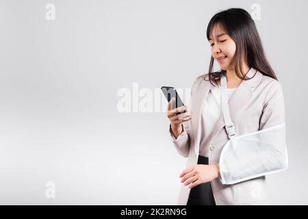 Woman confident smiling broken arm after accident and wear arm splint for treatment and hold smartphone Stock Photo