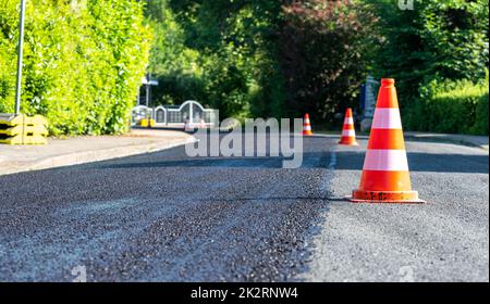 Construction cones marking part of road with a layer of fresh asphalt. Stock Photo