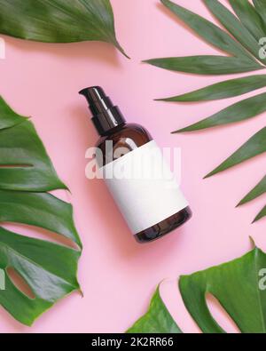 Brown one pump Bottle between tropical leaves on pink top view. Brand packaging mockup Stock Photo
