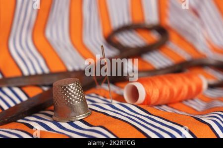 Orange Thread and Thimble on Orange and White Striped Fabric Stock Photo