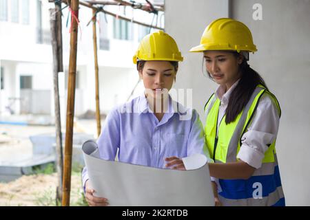 Young engineer in a construction helmet and safety vest explaining to project owner about a floor plan. Work environment of engineers at the construction site of housing projects. Stock Photo