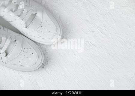 White leather sneakers stand in the left corner on a white textured background Stock Photo