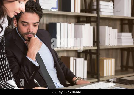 Business people working together and discussing on new project. Businessman sitting in office desk while business woman writing and standing besides him.. Stock Photo