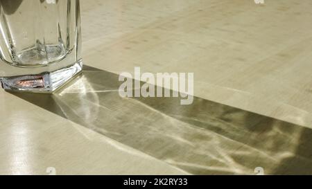 Drinking glass with caustic light effects on a wooden table. Stock Photo