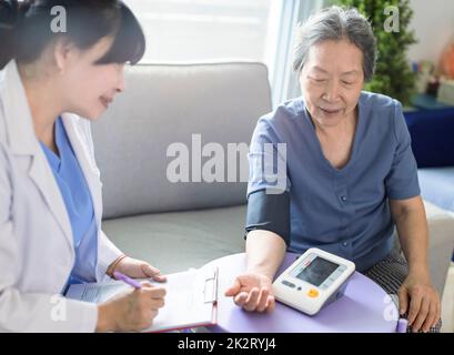 Asian caregiver doctor examine older patient use blood pressure gauge. Stock Photo