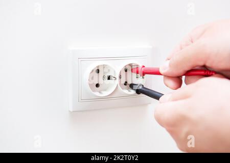 Measuring the voltage in the socket with a professional digital multimeter. Profession electrician, the process of installing sockets. Close-up, selective focus, noise. Stock Photo